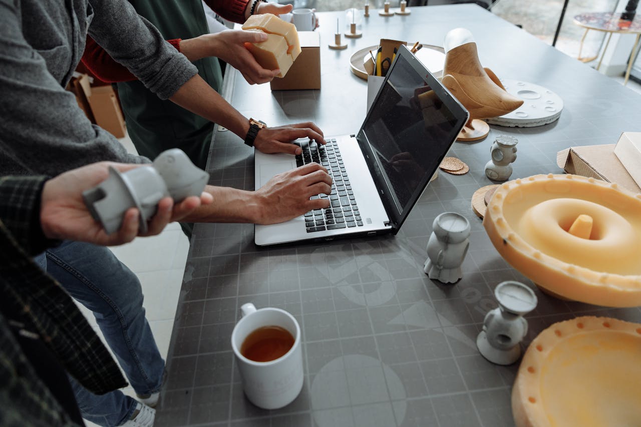 why-choose-us Hands on laptop in a creative workspace with 3D models and prototypes.